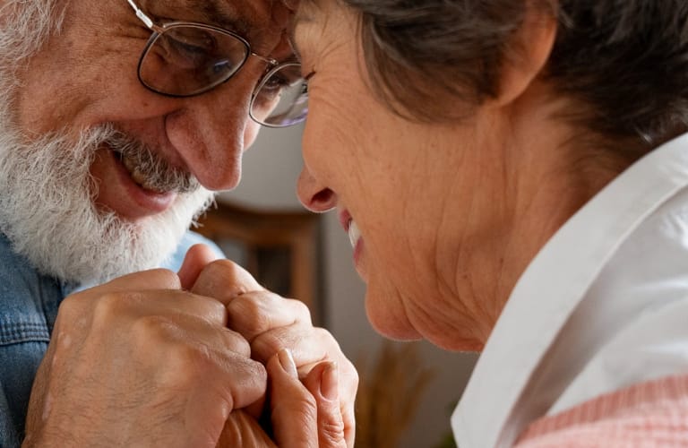 An elderly couple holding hands and resting their foreheads on each other