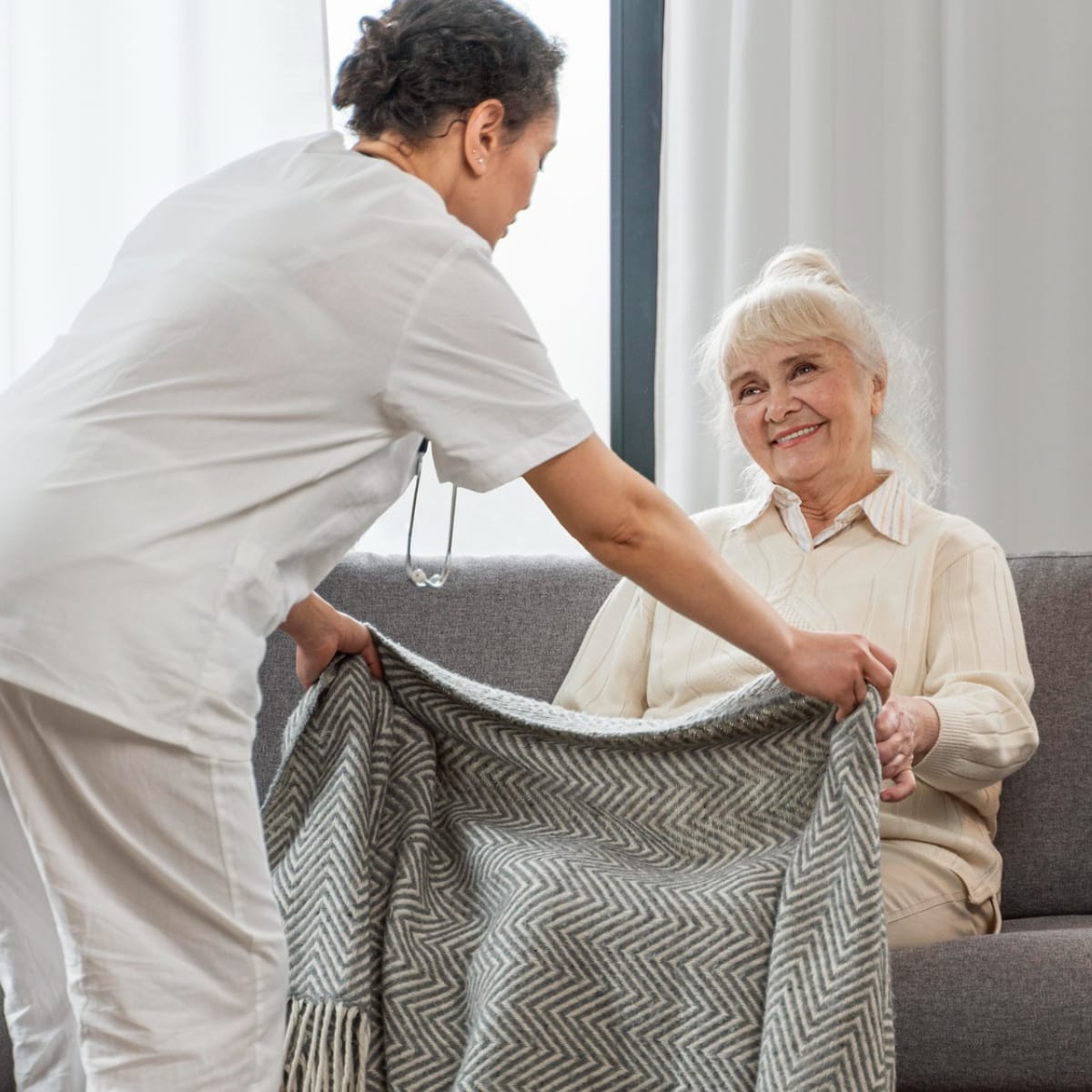 Caregiver placing blanket over elderly womans lap